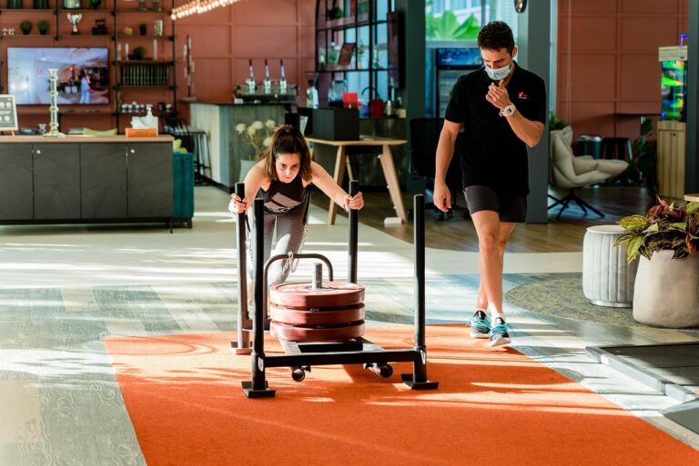 Entrenador junto a un trineo de empuje cargado en el gimnasio